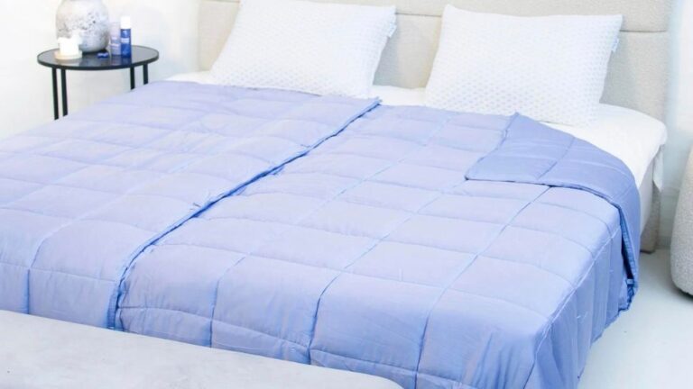 Tyngdedyne miljø med tyngdedynen "NapCool" fra TheNap. Tyngdedynen er i blå og er placeret på en seng som er redt op.